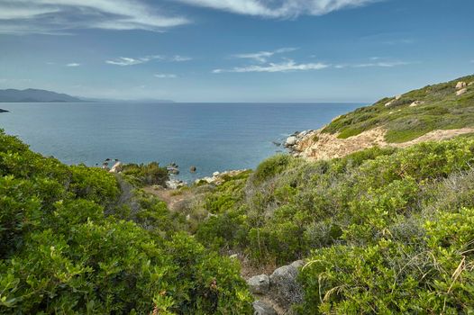 A glimpse of a southern coastline of Sardinia rich in green shrubs overlooking the blue and pristine sea.