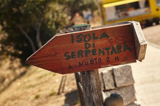 Small wooden indication board with written "Island of Serpentara, swimming 2 hours". A small sign that tells tourists of this zzona of southern Sardinia how to reach the island in the middle of the sea in front of it.