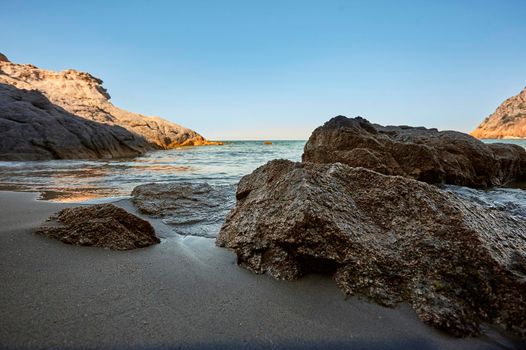 Beautiful seascape with wide-angle shot of the exit from a cave with the sea and the shore of the beach in the foreground, the sea to the horizon in the background and to the right a rock that merges with the sea. Symbol of vacations and natural beach.