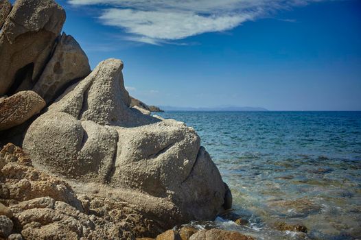 A particular rock with sinuous and undulating forms with the background of the azure and crystalline Mediterranean sea during the summer.