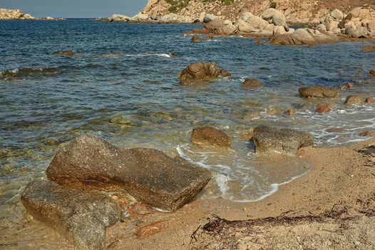 Some pebbles resting on the shore of the sea where the crystalline water meets with the sand of the sea.