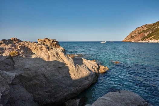 A natural promontory made of rock, it is the master in a Mediterranean seascape with some luxury boats on the horizon.