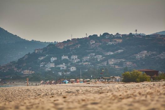 Panorama with small mountain full of houses overlooking the beach with some tourists on the horizon.