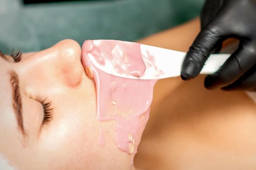 The cosmetologist applying an alginic mask to the face of a young woman in a beauty salon