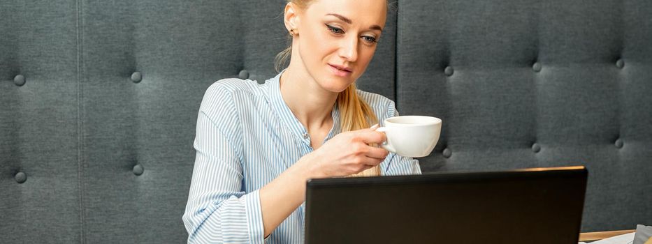 Portrait of a young businesswoman using laptop sitting at the table with a cup of coffee in a cafe