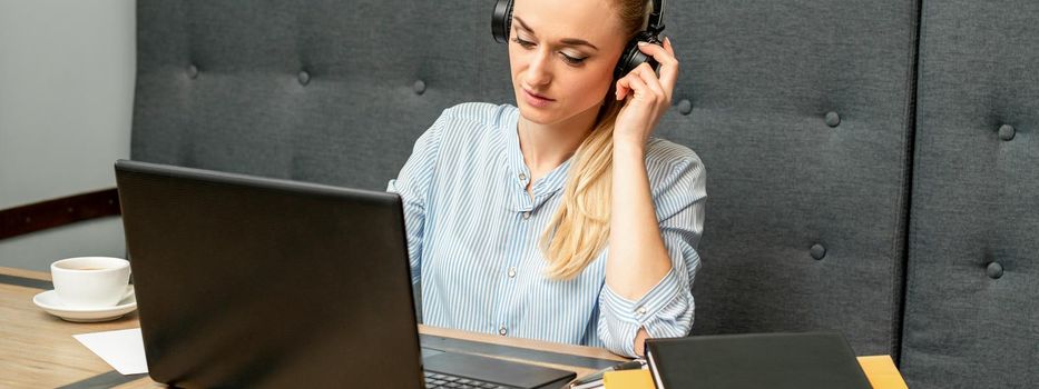 Beautiful young caucasian woman with headphones and laptop sitting at the table in a cafe