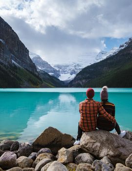 Lake Louise Banff national park is a lake in the Canadian Rocky Mountains. A young couple of men and women sitting on a rock by the lake during a cold day in Autumn in Canada