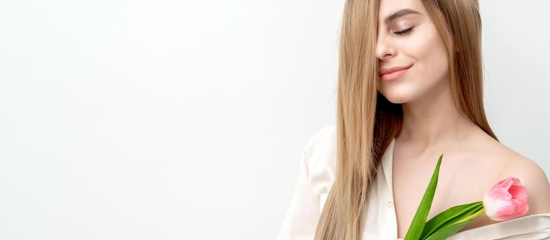 A portrait of a happy young caucasian woman with closed eyes and one pink tulip against a white background with copy space