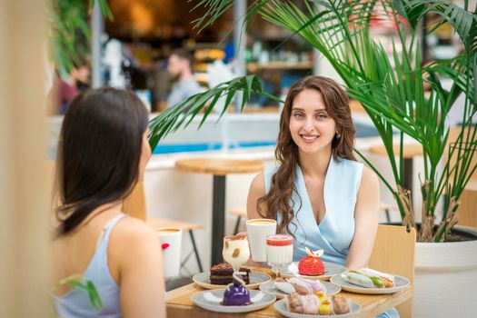 Two beautiful young caucasian women drink coffee sitting at the table in cafe outdoor