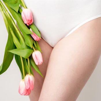 Bikini area of a young woman wearing a white underwear with pink tulips on white background
