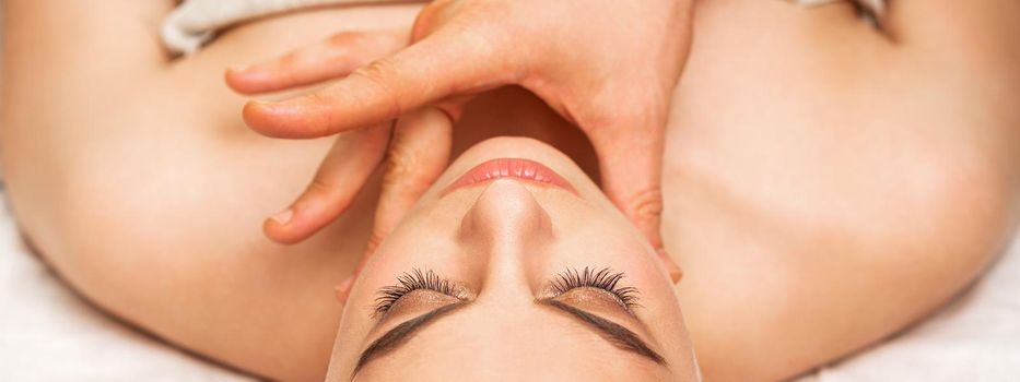 Chin or neck massage of a young woman by the hand of a male massage therapist in a spa salon