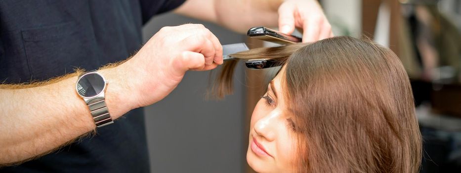 A male hairdresser is straightening the hair of the young woman in a beauty salon