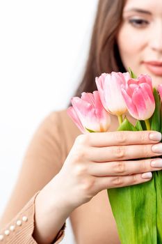 A young caucasian woman holds pink tulips in her hands against a white background