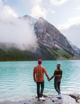 Lake Louise Banff national park, is a lake in the Canadian Rocky Mountains. A young couple of men and women standing by the lake during a cold day in Autumn in Canada