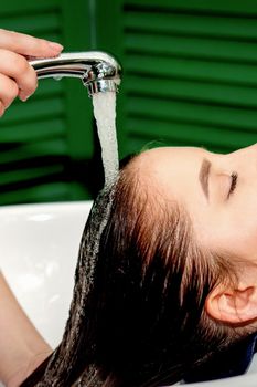 Side view photo of a young caucasian woman receiving washing hair in a hair salon