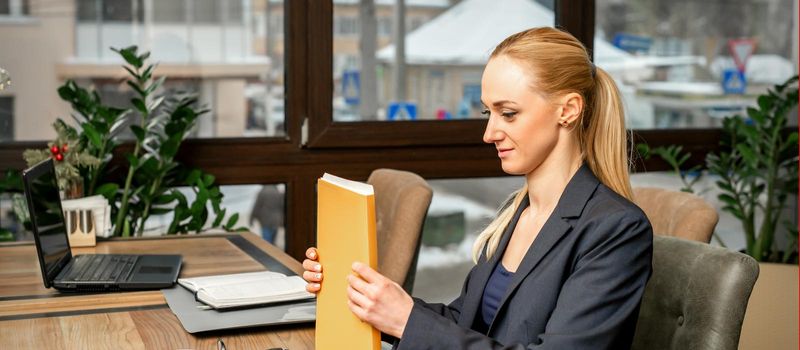 Beautiful young caucasian businesswoman holding a folder with documents sitting at the table in office or cafe