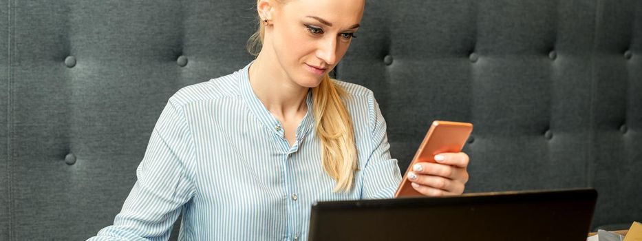 Young businesswoman using smartphone sitting at the table with laptop in cafe