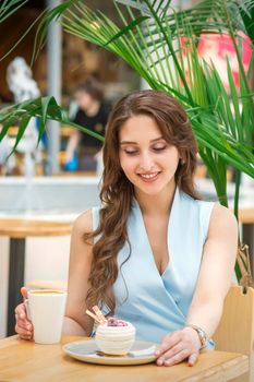 A beautiful young caucasian woman sitting at the table with cakes and a cup of coffee in cafe outdoor