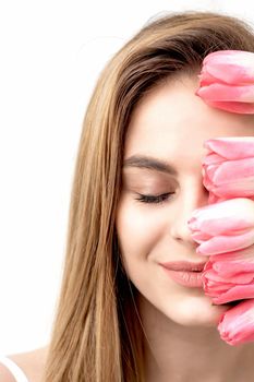 A portrait of a happy young caucasian woman with closed eyes and pink tulips cover her face against a white background