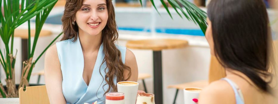 Two beautiful young caucasian women drink coffee sitting at the table in cafe outdoor