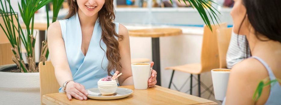 Two beautiful young caucasian women drink coffee sitting at the table in cafe outdoor