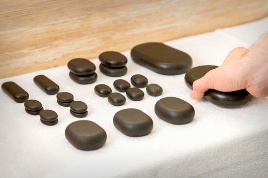 Hand of massage therapist taking massage stones from the table before massage procedures