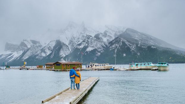 Minnewanka lake in the Canadian Rockies in Banff Alberta Canada with turquoise water, Lake Two Jack in the Rocky Mountains of Canada. a couple of men and women hiking by the lake during snow weather