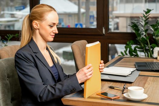 Beautiful young caucasian businesswoman holding a folder with documents sitting at the table in office or cafe