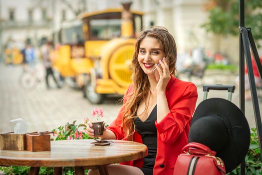Beautiful young caucasian tourist woman talks on the phone sitting at the table in the street cafe in a European city