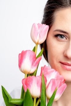 Half face portrait of a happy young caucasian woman with pink tulips against a white background