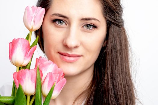 Portrait of a happy young caucasian woman with pink tulips against a white background