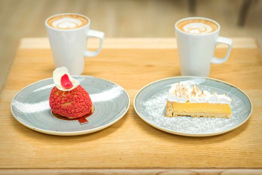 Two white cups of coffee with different pieces of cakes in saucers on the wooden table