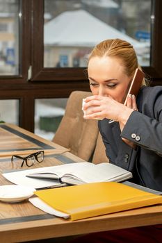 Busy young businesswoman drinking coffee talking on the smartphone at work in a cafe