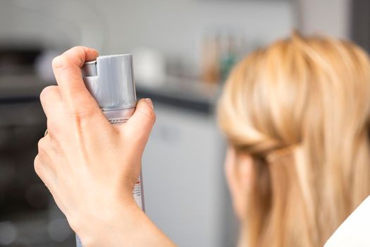 Closeup of hair spray in the hand of hairstylist while fixing blonde hair of the young woman in a beauty salon