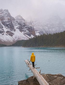 Lake moraine during a cold snowy day in Autumn in Canada, Beautiful turquoise waters of the Moraine lake with snow. couple of men and women in yellow raincoat jacket during snow