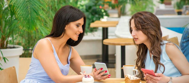 Two beautiful young women together watching something on the phone at the table in a cafe