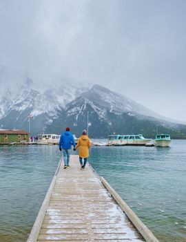 Minnewanka lake in the Canadian Rockies in Banff Alberta Canada with turquoise water, Lake Two Jack in the Rocky Mountains of Canada. a couple of men and women hiking by the lake during snow weather