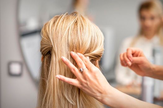 Back view of the female hand of hairdresser models a hairstyle of a young blonde woman in a hair salon