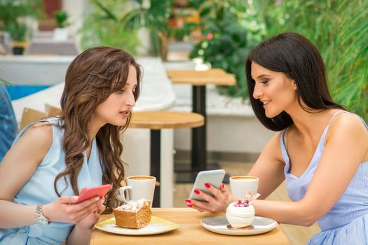 Two beautiful young women together watching something on the phone at the table in a cafe