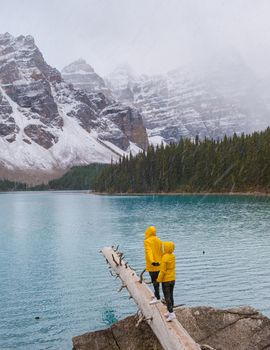 Lake moraine during a cold snowy day in Autumn in Canada, Beautiful turquoise waters of the Moraine lake with snow. couple of men and women in yellow raincoat jacket during snow