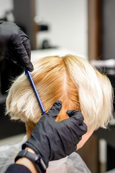 Hairdresser combing female short blonde hair before dyeing in a hair salon