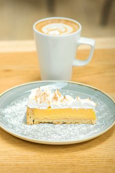 White cup of coffee with piece of cake in saucer on the wooden table