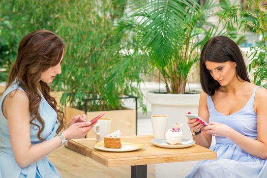 Two young women looking their smartphones while sitting in a cafe. Technology people addictions