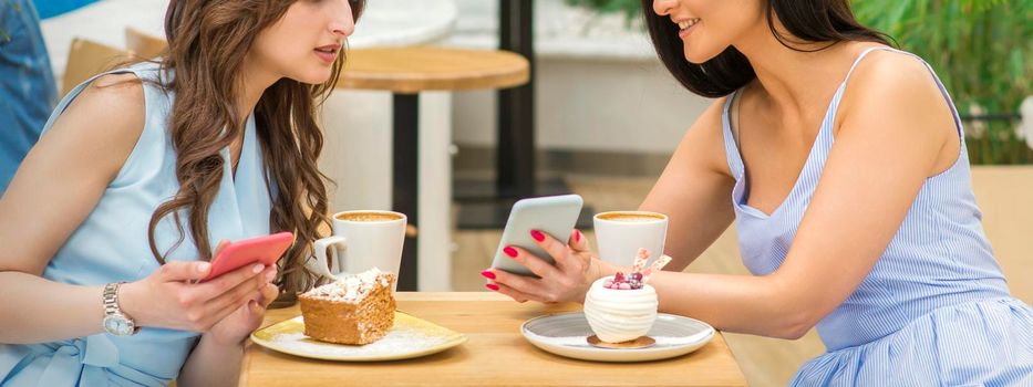 Two beautiful young women together watching something on the phone at the table in a cafe