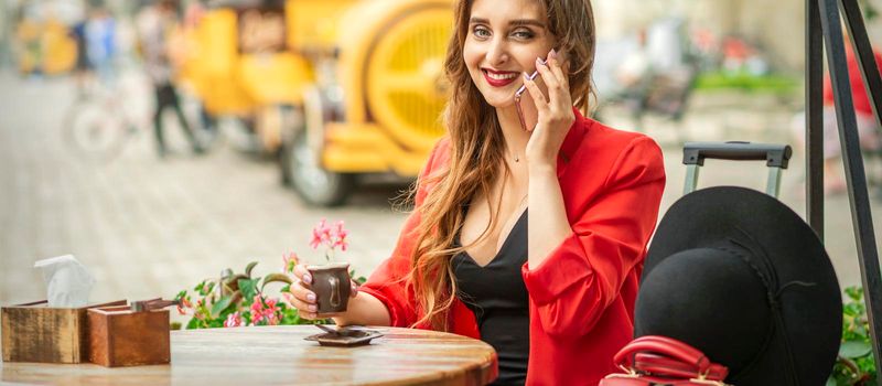 Beautiful young caucasian tourist woman talks on the phone sitting at the table in the street cafe in a European city