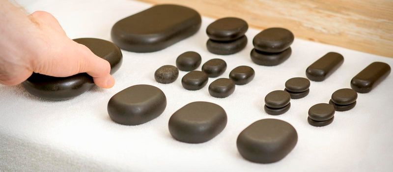 Hand of massage therapist taking massage stones from the table before massage procedures