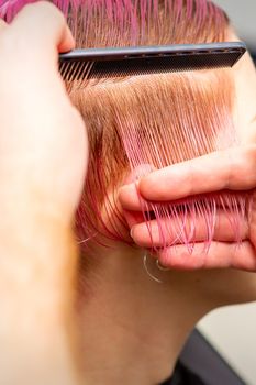 Male hairdresser combing hair making short pink hairstyle for a young caucasian woman in a beauty salon