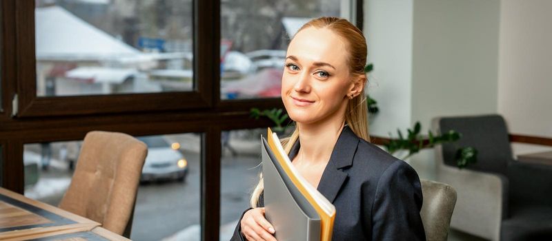 Beautiful young caucasian businesswoman holding a folder with documents sitting at the table in office or cafe