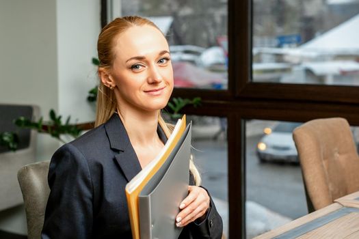 Beautiful young caucasian businesswoman holding a folder with documents sitting at the table in office or cafe