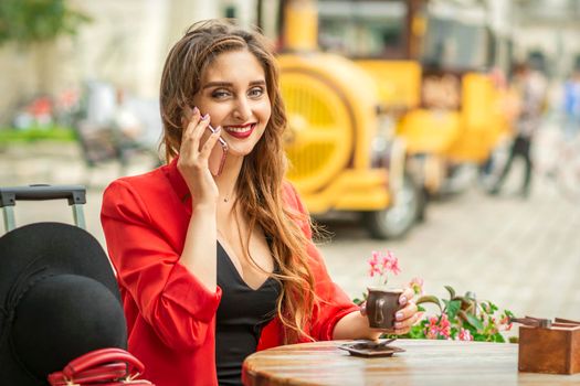 Beautiful young caucasian tourist woman talks on the phone sitting at the table in the street cafe in a European city